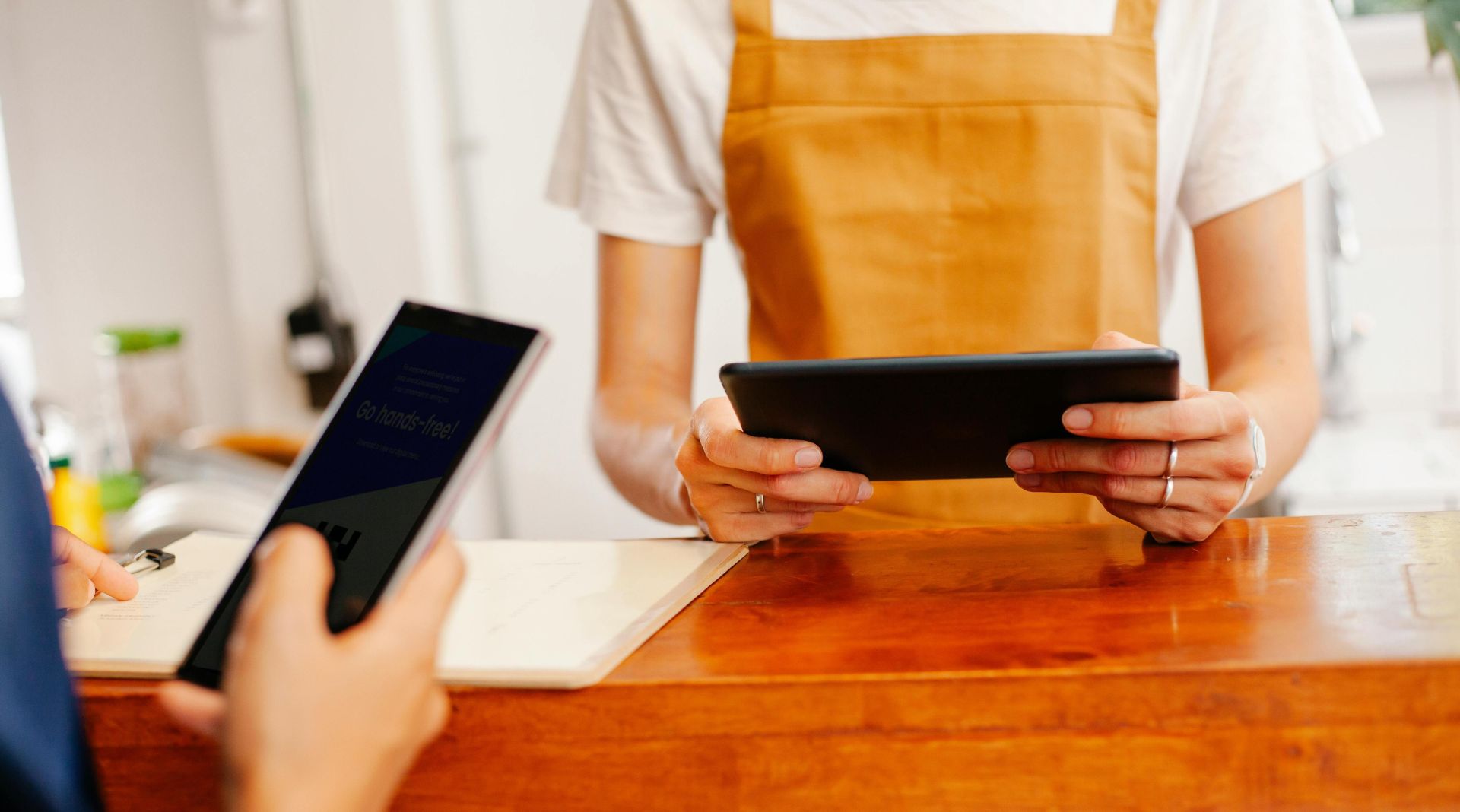 A barista in an apron uses a tablet in a small cafe. Customer interaction at the counter.